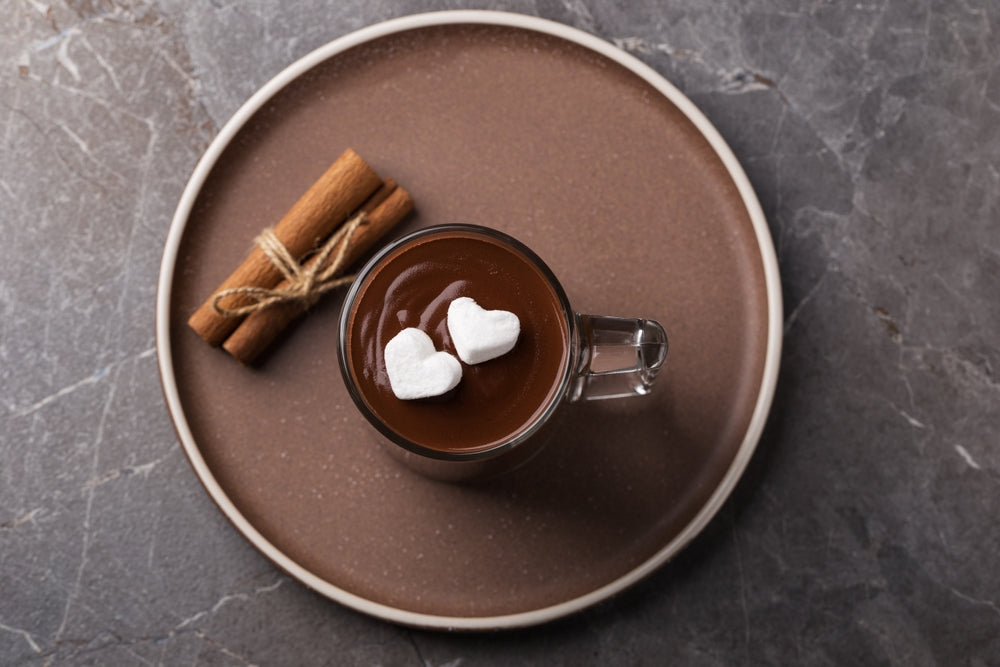 Hot chocolate with heart shaped marshmallows on a brown serving tray resting on a marble countertop 