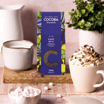 Cocoba 45% Dark Milk Drinking Chocolate Flakes in smart blue packaging, with a hot chocolage and jug of milk next to it.