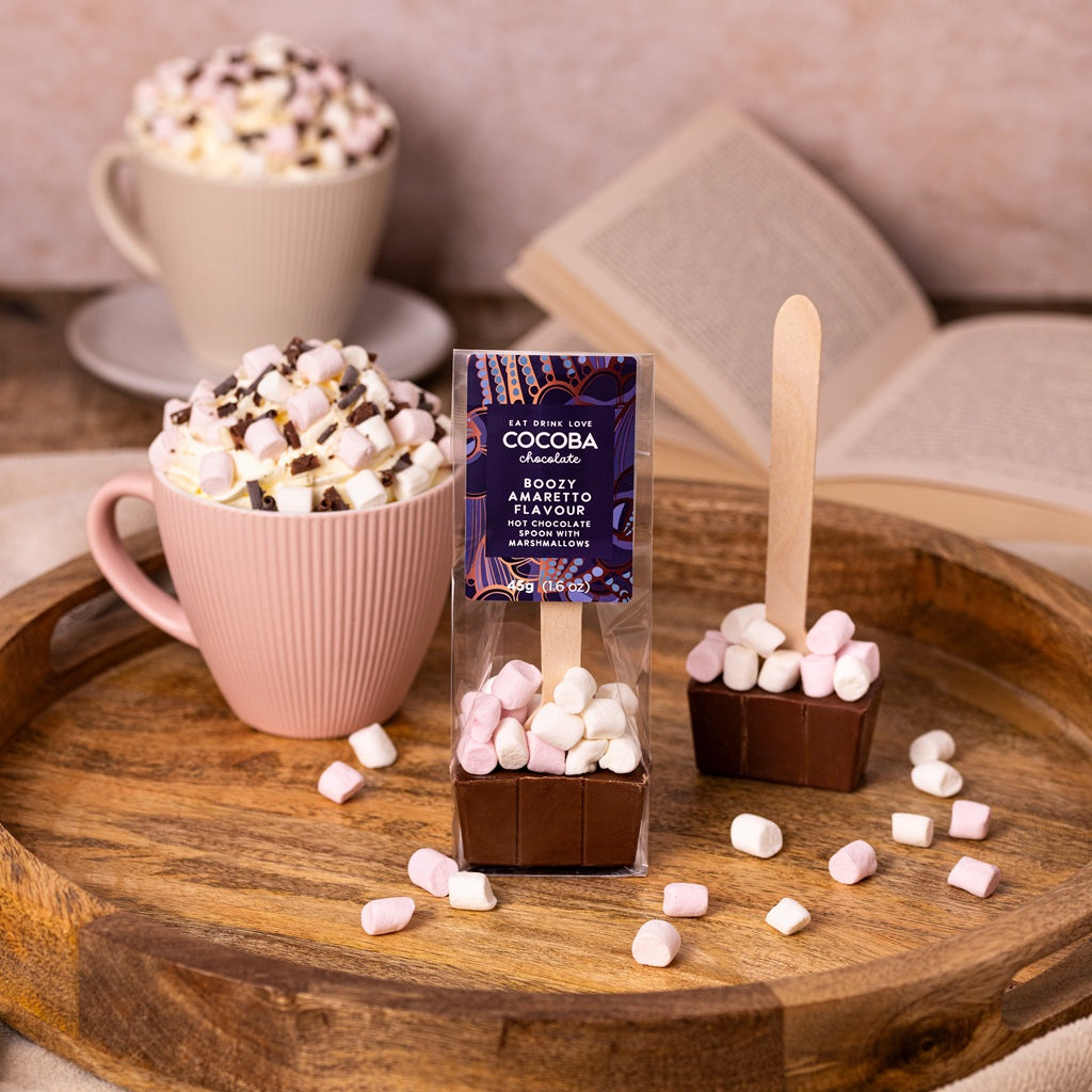 Amaretto flavoured milk hot chocolate spoon, with mini marshmallows, next to a delicious mug of hot chocolate and a reading book  