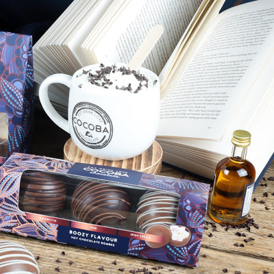 Cocoba hot chocolate bombs with a Cocoba mug, a book, and liqueur bottle