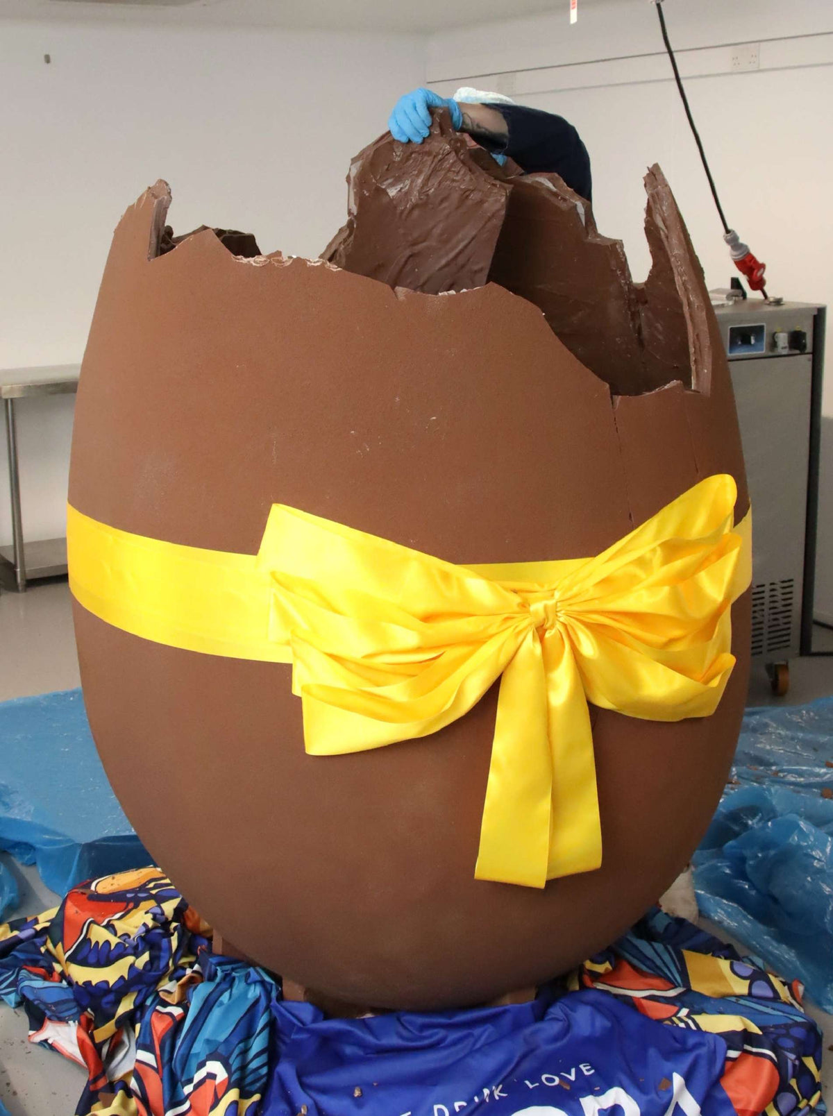 Large chocolate egg with a yellow ribbon on a colorful surface.