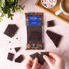 Cocoba chocolate bar with packaging, surrounded by broken pieces and a cup of coffee on a light surface.