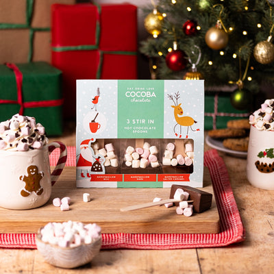 Cocoba hot chocolate spoons with Christmas decorations and hot chocolate in the background