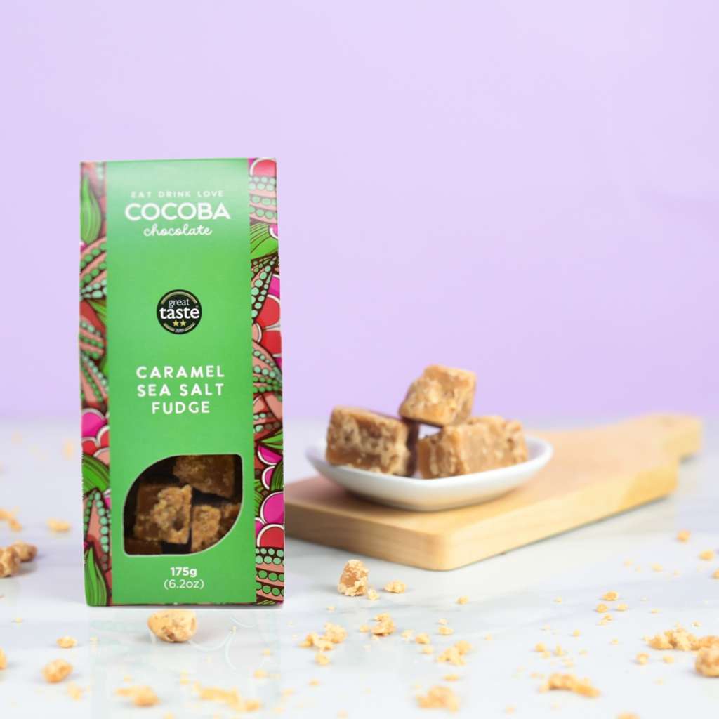 Cocoba Caramel Sea Salt Fudge packaging with fudge pieces on a plate and scattered around on a light purple background.