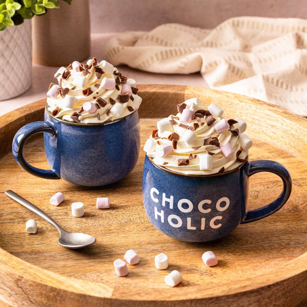 Two blue mugs from Cocoba labeled 'CHOCOHOLIC', with hot chocolate and marshmallows on a wooden tray.