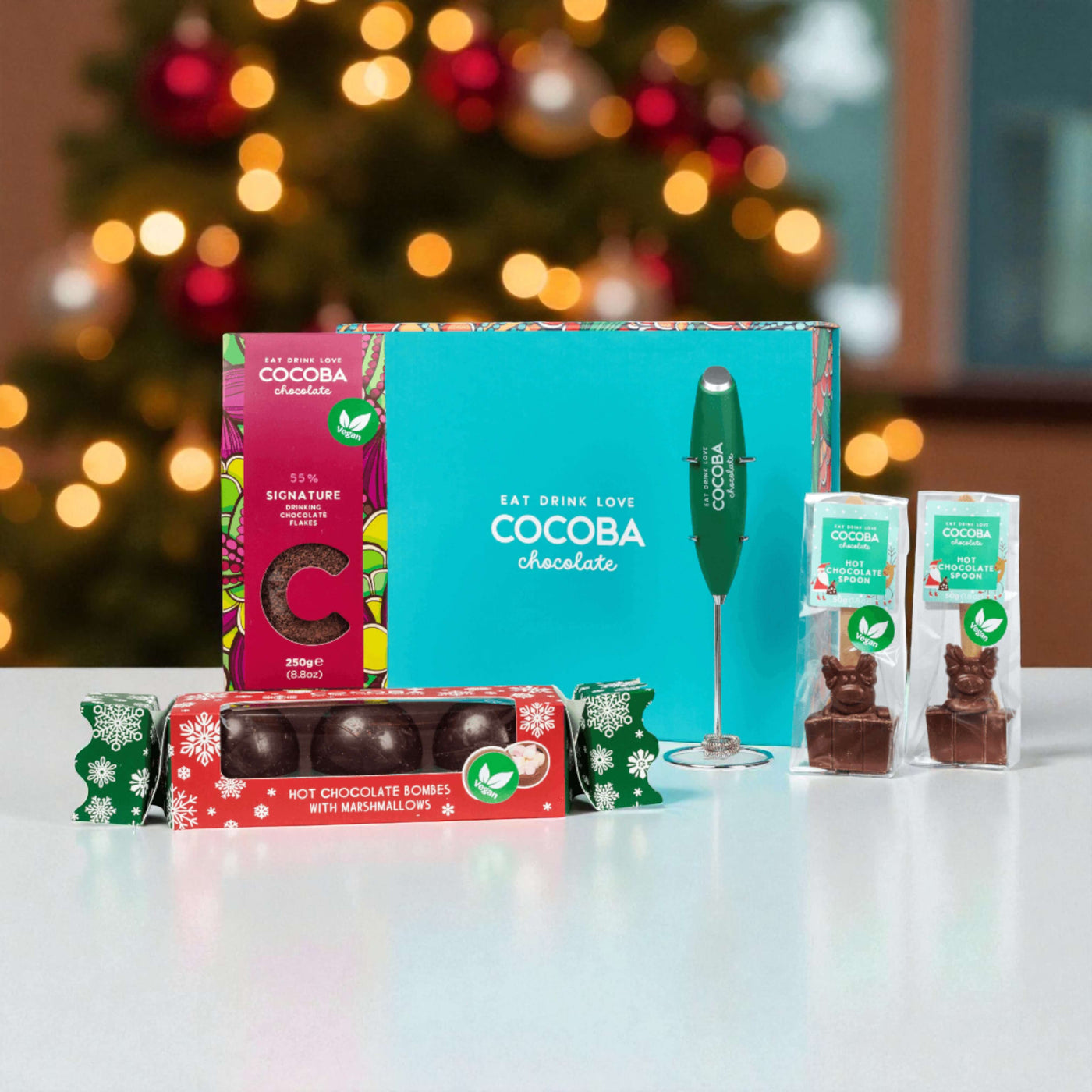 Cocoba chocolate products on a table with a blurred Christmas tree in the background