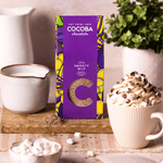 35% smooth milk drinking chocolate flakes next to a hot chocolate and jug of milk on a wooden board. 