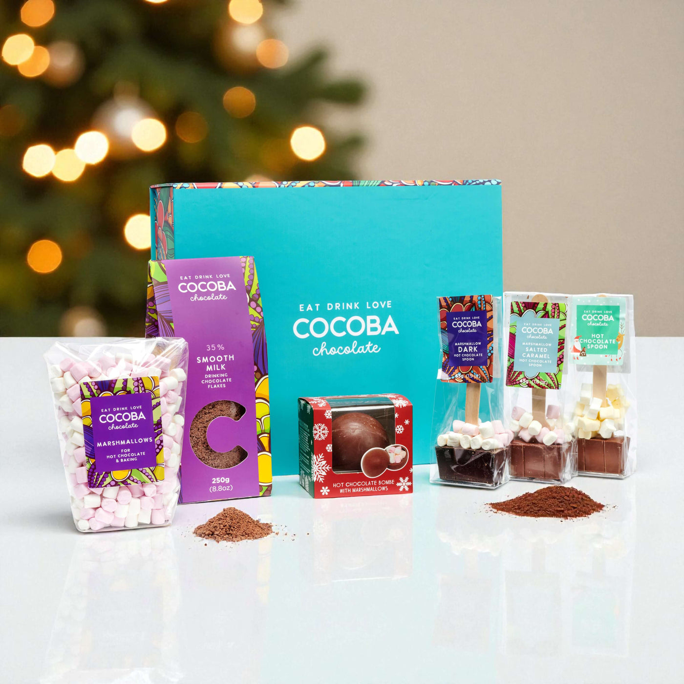 Cocoba chocolate products including bars and packets on a table with a blurred Christmas tree in the background.