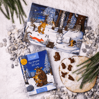 Advent calendar and book titled 'The Snow Fell Last' on a snowy surface with cookies.