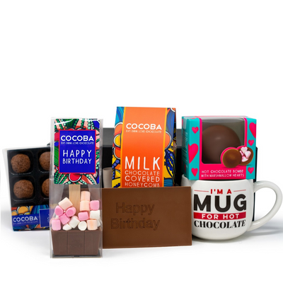 A collection of chocolate gifts including a 'Happy Birthday' engraved chocolate bar, milk chocolate covered honeycomb, salted caramel truffles, a hot chocolate bombe with marshmallows, and a mug with the text 'I'm A Mug For Hot Chocolate'. All items are presented in colorful packaging.
