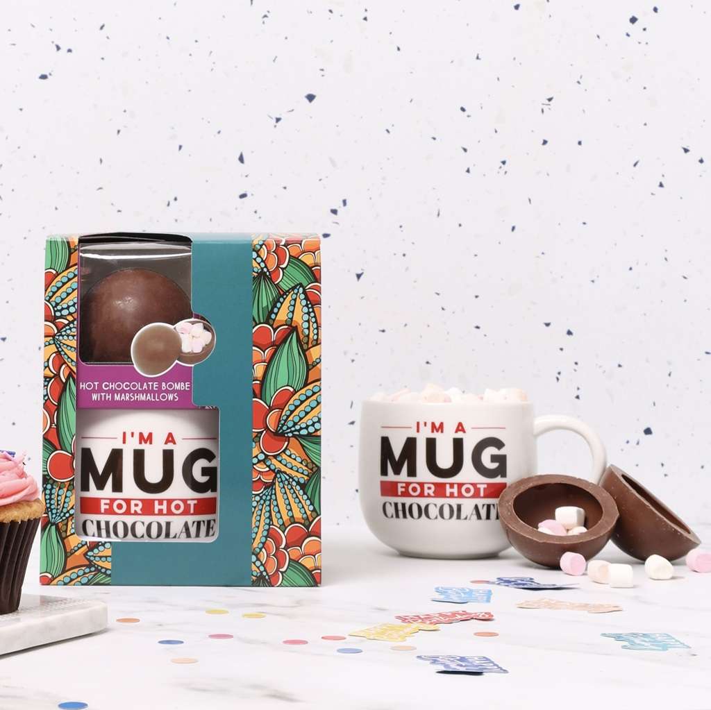 Hot chocolate mug and bomb gift set on a white surface with a colorful box.