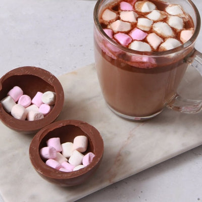 Hot Chocolate Bombe cracked open with marshmallows inside and a mug of hot chocolate next to it