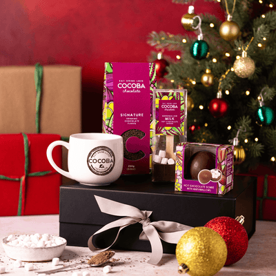 COCOBA hot chocolate and mug set with Christmas tree and presents in the background