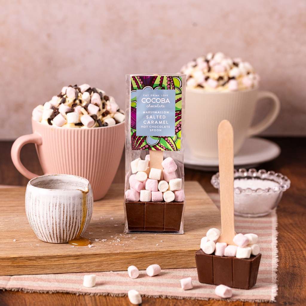 Hot chocolate bomb with marshmallows on a wooden surface with mugs and a package in the background.