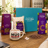 Cocoba milk chocolate buttons, 35% milk hot chocolate flakes, marshmallows and a Cocoba Mug in a bright Cocoba gift box on a wooden table.