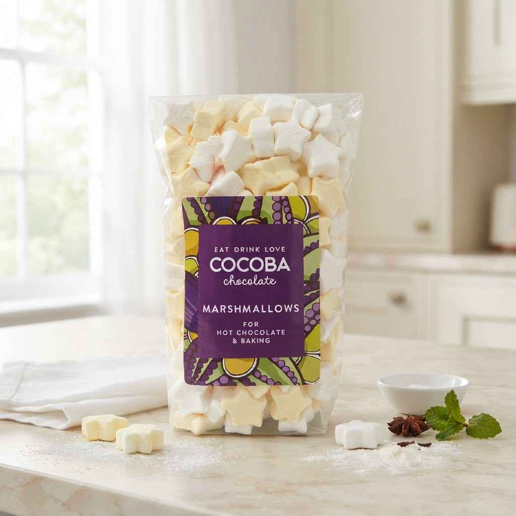A bag of Cocoba Chocolate marshmallows for hot chocolate and baking, displayed on a marble kitchen counter with a few loose marshmallows and small garnish props.