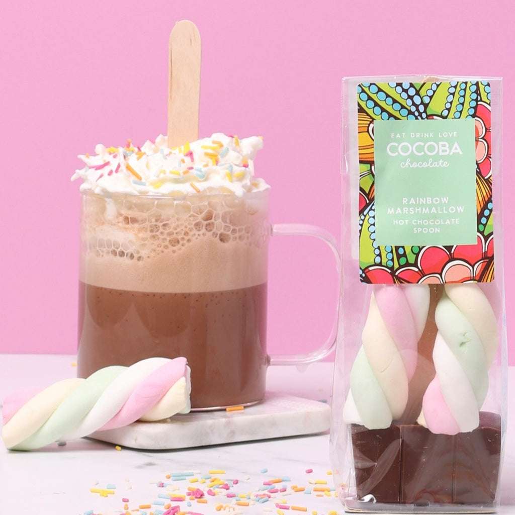 Milk chocolate Hot chocolate spoon with pastel coloured marshmallows and a colorful COCOBA package on a pink background