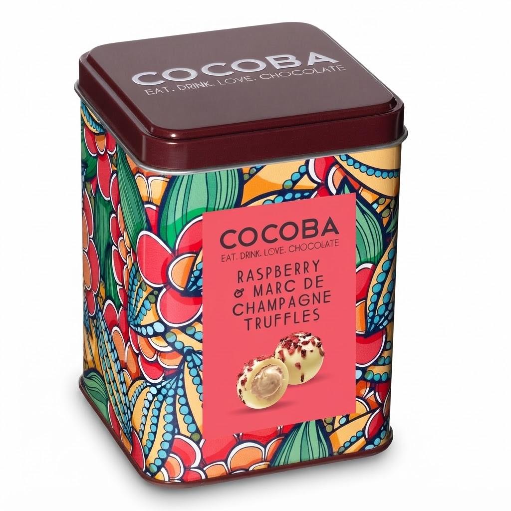 A square metal tin of COCOBA Raspberry & Marc de Champagne Truffles, featuring a vibrant multicolor floral and paisley pattern, a dark brown lid, and a pink label on a white background.