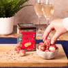 Raspberry and Marc de Champagne Truffles Gift Tin on a wooden board with two glasses of champagne in the background. 