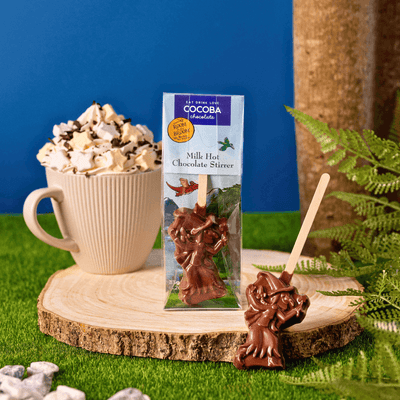 Milk hot chocolate stirrer with packaging on a wooden stand with a cup of hot chocolate.