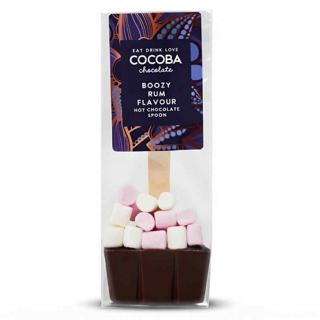 A packaged chocolate hot spoon in a clear plastic bag with a printed label. The product shows a dark brown chocolate base topped with pink and white marshmallows, with a wooden spoon handle visible inside.