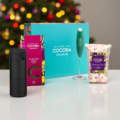 Cocoba chocolate products including a black thermos, packaging, and a bag of marshmallows with a Christmas tree in the background.