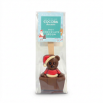 A packaged chocolate hot chocolate spoon featuring a teddy bear wearing a Santa hat and red sweater, sitting in a small chocolate box. The item is in clear retail packaging with a printed label that reads 'COCOBA chocolate HOT CHOCOLATE SPOON'.
