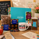 Teacher appreciation gift set with COCOBA chocolate, a mug, and stationery on a wooden surface.
