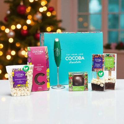 Vegan_Hot_Chocolate_Frother_Collection_Gift_Box on a white surface with a christmas tree in the background