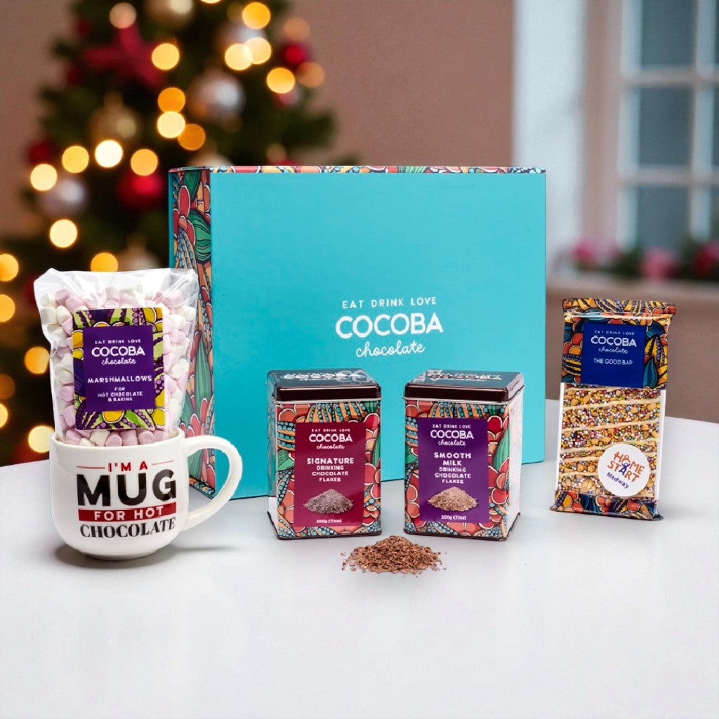 Cocoba chocolate products including a mug, boxes, and packets on a table with a blurred Christmas tree in the background.