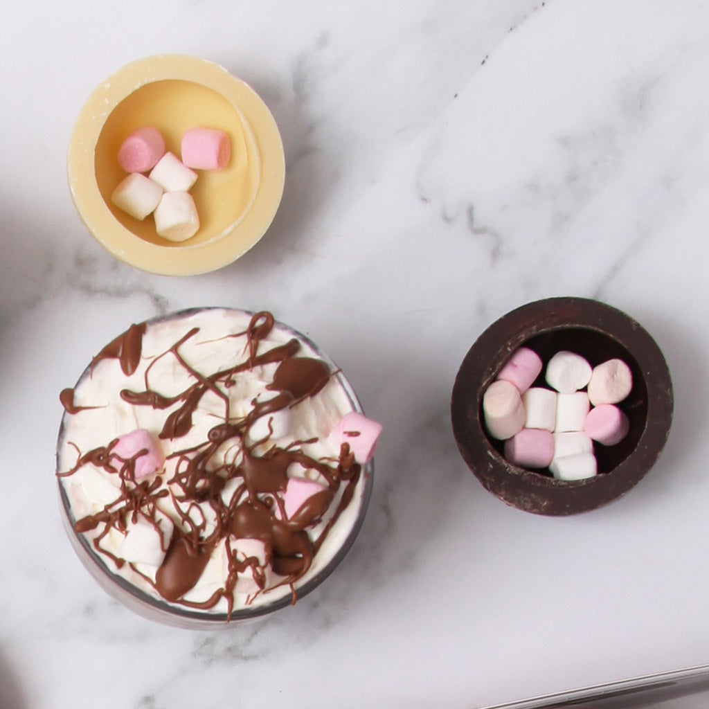 Hot chocolate with marshmallows and chocolate drizzle with Milk and White Hot Chocolate Bombes Cracked open
