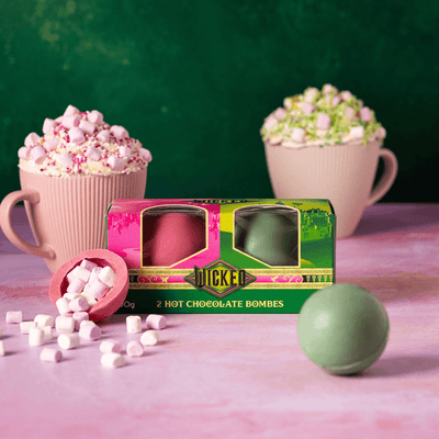 Hot chocolate bombs with a box labeled 'Jumbo' on a pink surface with a green background.
